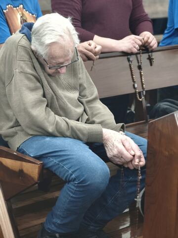 Homem rezando o terço nos bancos da igreja