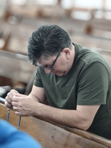 Homem em oração com o terço nas mãos
